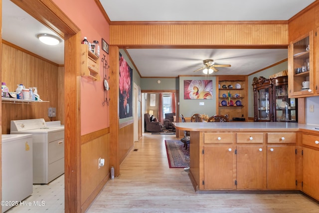 kitchen featuring ceiling fan, light wood-style floors, wooden walls, separate washer and dryer, and ornamental molding