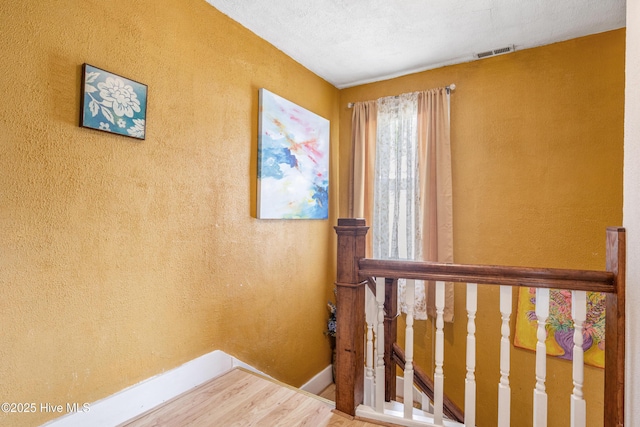 staircase featuring visible vents, a textured wall, and wood finished floors