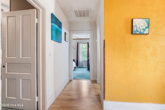 hall with baseboards, visible vents, and wood finished floors