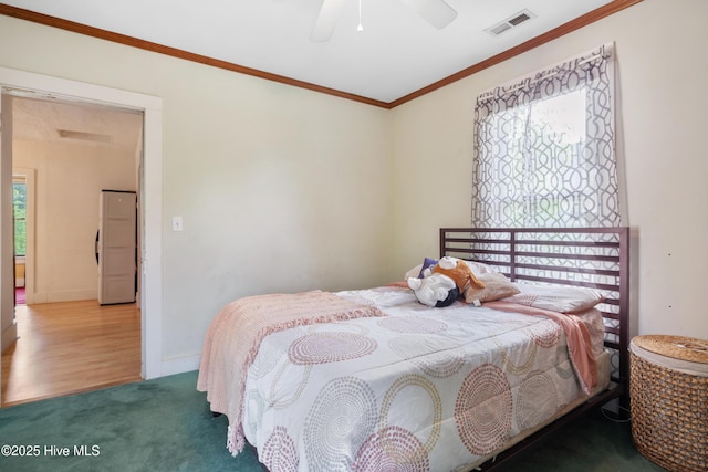 bedroom featuring freestanding refrigerator, ornamental molding, carpet flooring, visible vents, and a ceiling fan