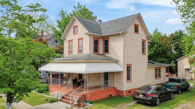 victorian-style house featuring covered porch, a shingled roof, a front yard, and crawl space