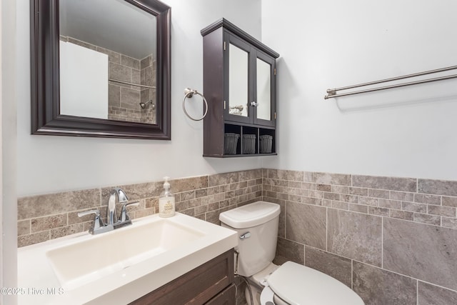 bathroom with tile walls, a wainscoted wall, vanity, and toilet