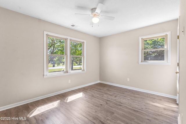 unfurnished room featuring baseboards, visible vents, wood finished floors, and a wealth of natural light
