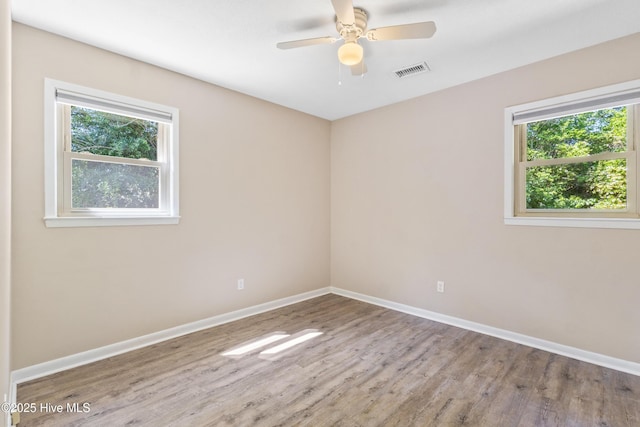 empty room with visible vents, baseboards, wood finished floors, and a wealth of natural light