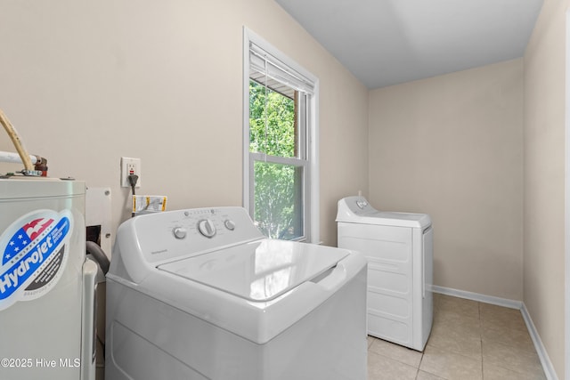 washroom featuring water heater, laundry area, light tile patterned flooring, and washer and clothes dryer