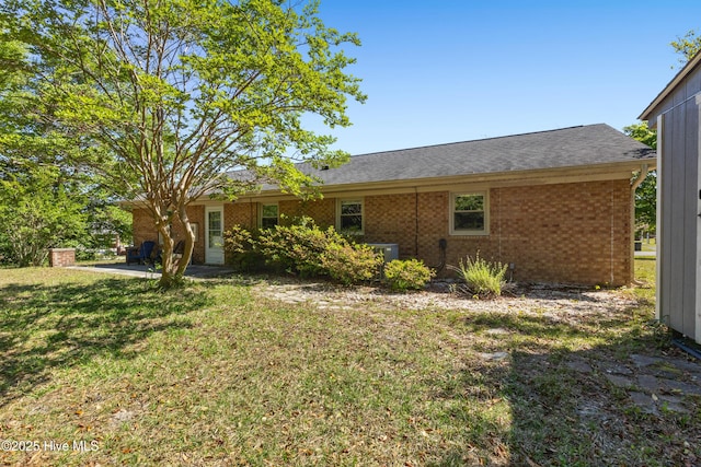 rear view of house with a lawn, central AC unit, brick siding, and a patio