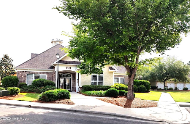 obstructed view of property with brick siding, a front lawn, and roof with shingles