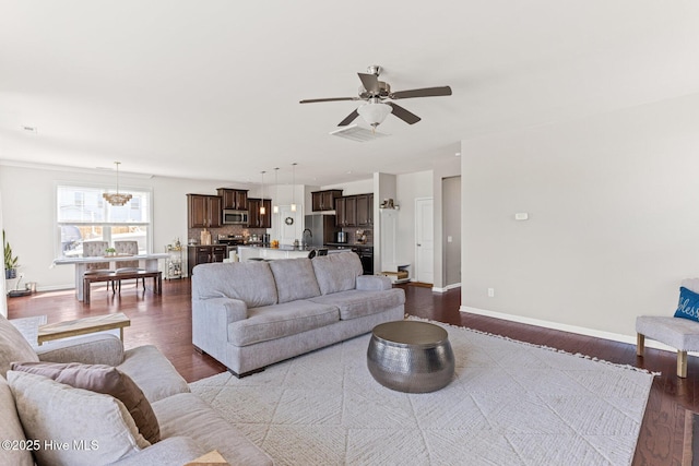 living area with baseboards, visible vents, dark wood-style floors, and ceiling fan with notable chandelier