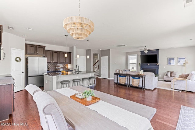 dining space with dark wood-style flooring, visible vents, ceiling fan with notable chandelier, and a fireplace