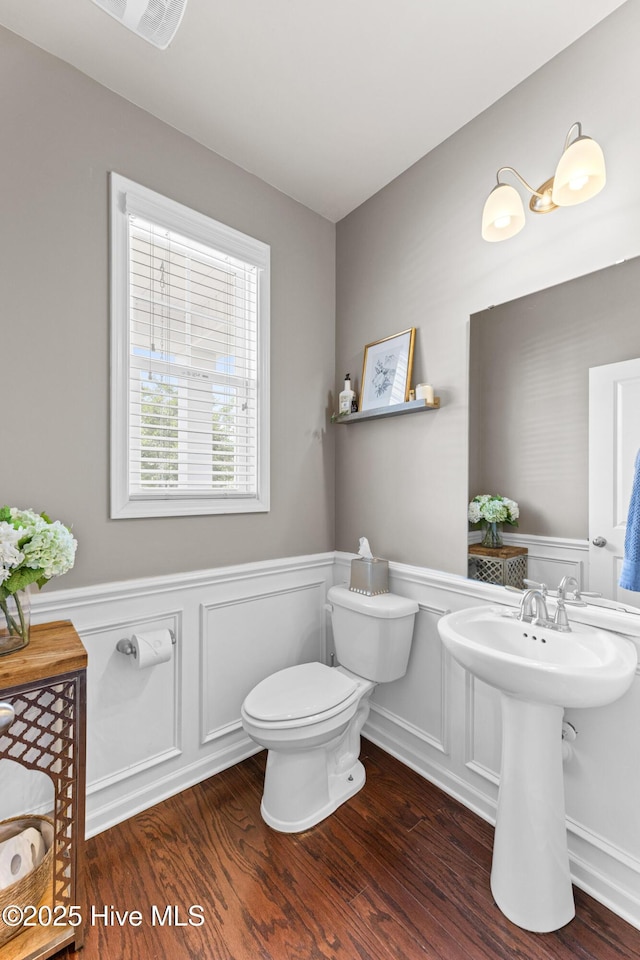 bathroom featuring toilet, wainscoting, wood finished floors, and a decorative wall