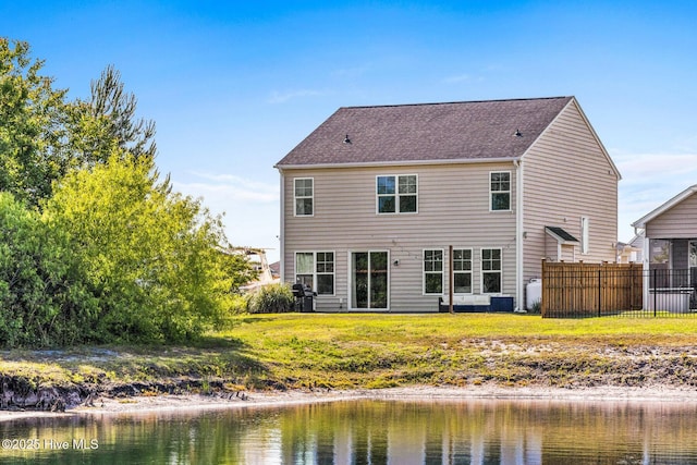 rear view of property featuring fence, a water view, and a lawn