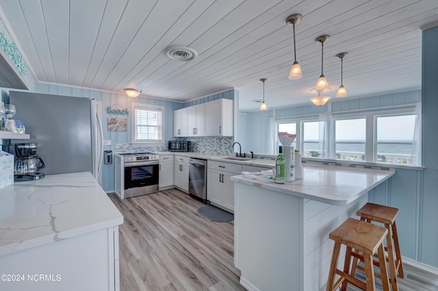 kitchen with light stone countertops, a sink, stainless steel appliances, a breakfast bar, and a peninsula