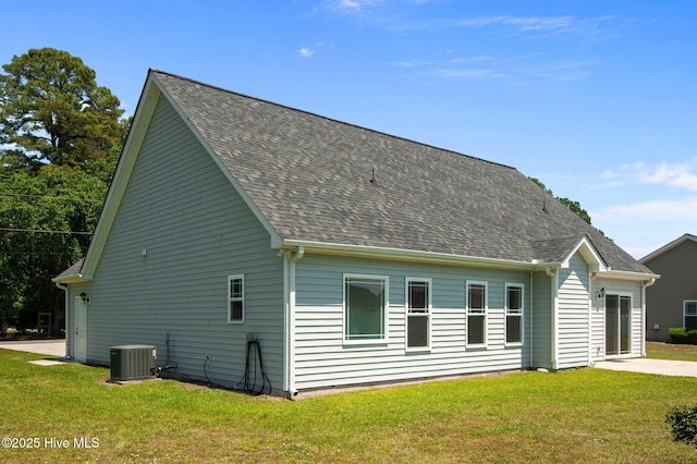 back of house featuring a lawn, a shingled roof, and cooling unit