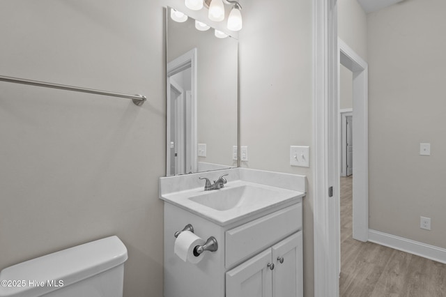 bathroom featuring vanity, baseboards, wood finished floors, and toilet