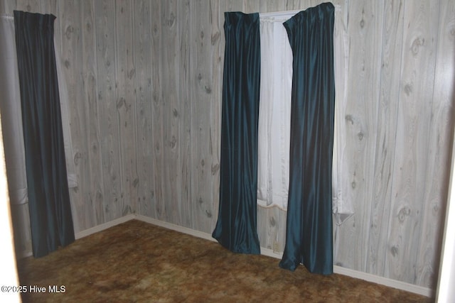 carpeted empty room featuring wooden walls and baseboards
