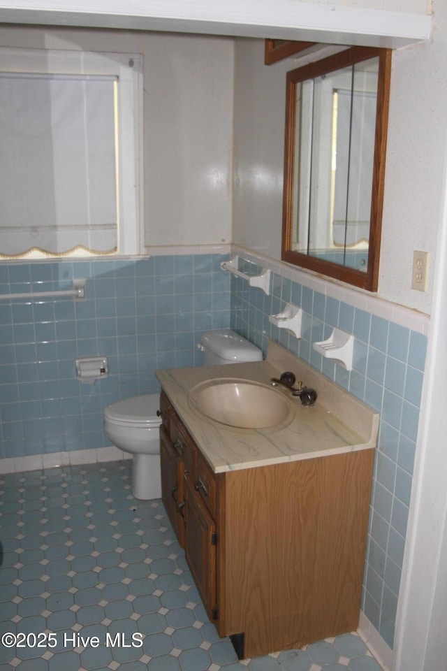 half bath featuring vanity, wainscoting, and tile walls