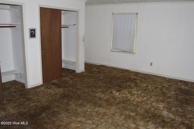 unfurnished bedroom with two closets, crown molding, and carpet