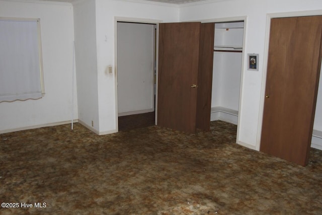 unfurnished bedroom with crown molding, baseboards, carpet, and two closets