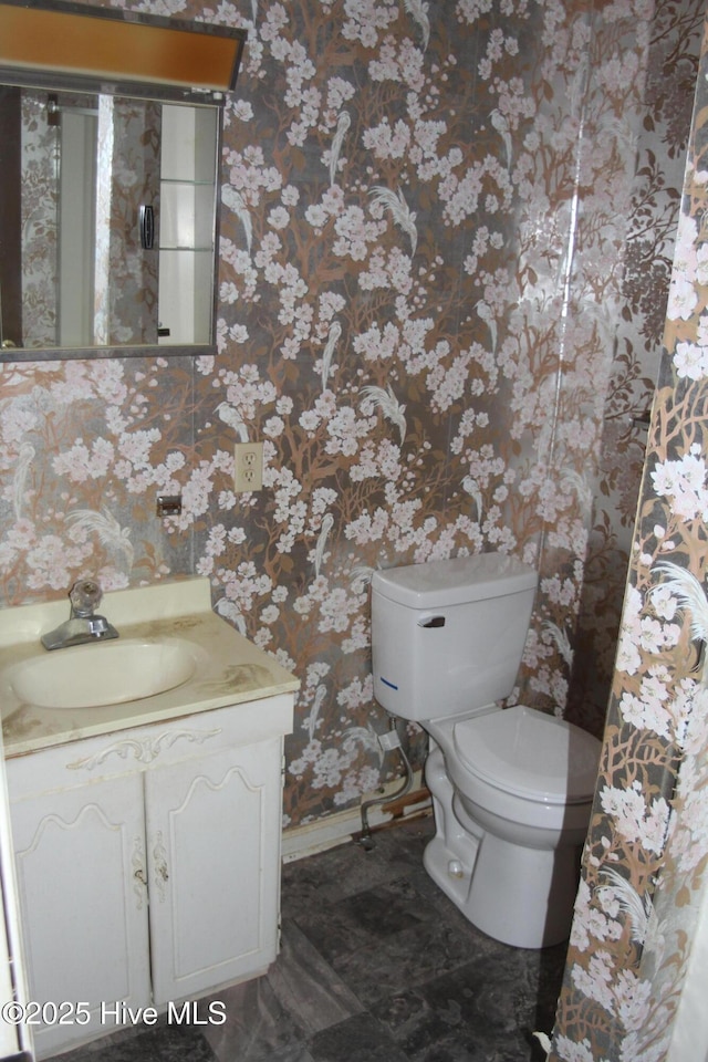 bathroom with baseboards, vanity, toilet, and wallpapered walls