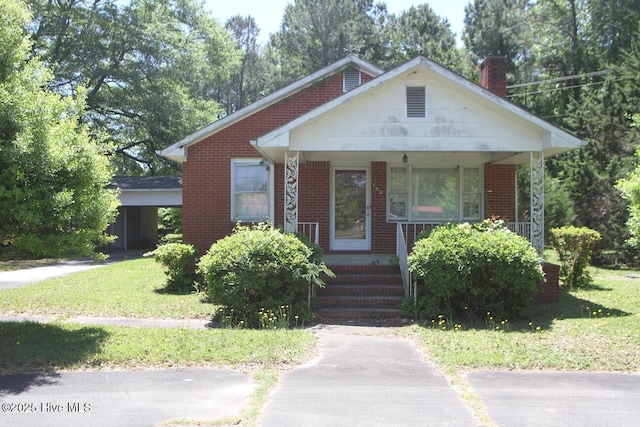bungalow-style house featuring covered porch, brick siding, a chimney, and a front yard