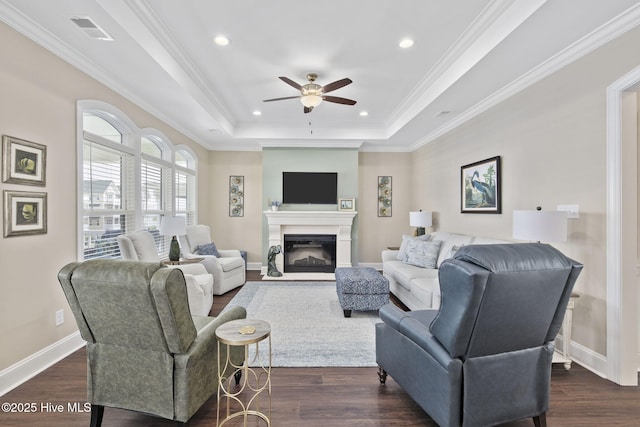 living room with ceiling fan, a glass covered fireplace, visible vents, dark wood-type flooring, and a tray ceiling