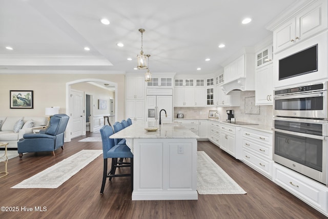 kitchen with double oven, a sink, arched walkways, open floor plan, and backsplash