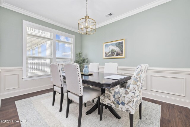 dining area with wood finished floors, an inviting chandelier, a wainscoted wall, visible vents, and crown molding