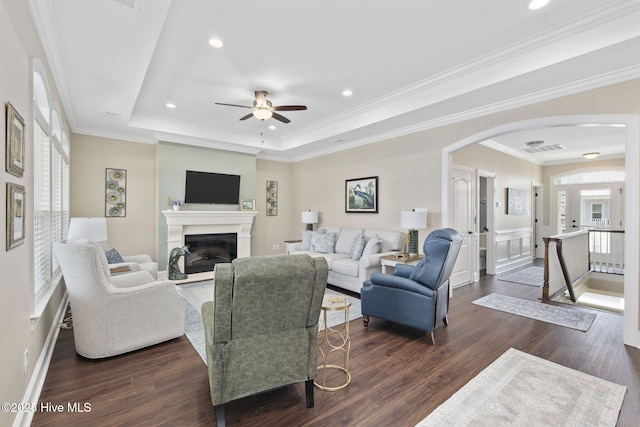 living room featuring arched walkways, a ceiling fan, dark wood-type flooring, and a tray ceiling