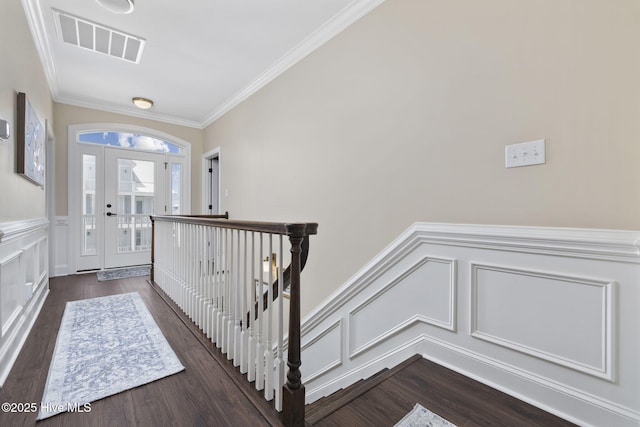 foyer featuring crown molding, a decorative wall, visible vents, a wainscoted wall, and wood finished floors