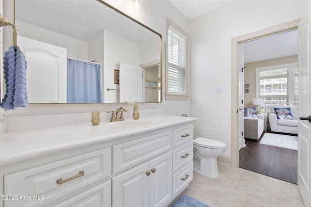 ensuite bathroom with tile patterned floors, toilet, vanity, and plenty of natural light