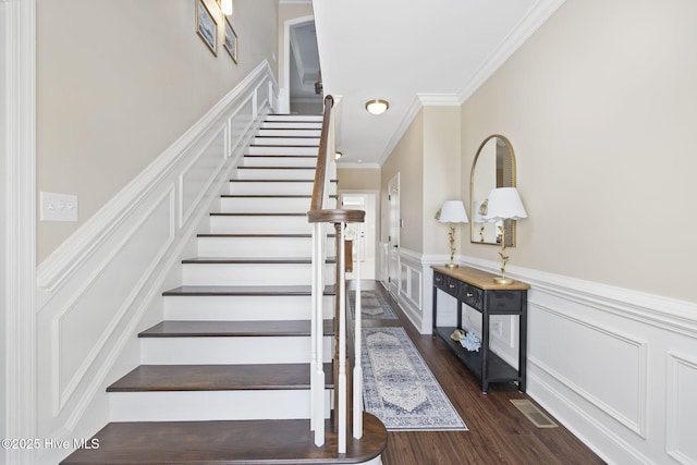 stairs with crown molding, a wainscoted wall, visible vents, a decorative wall, and wood finished floors