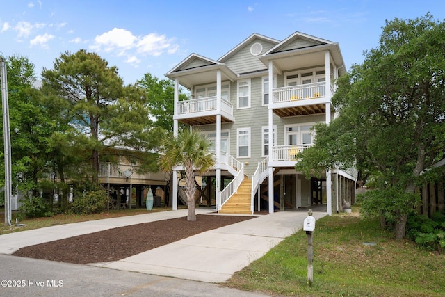 raised beach house with a porch, stairway, a balcony, a carport, and concrete driveway