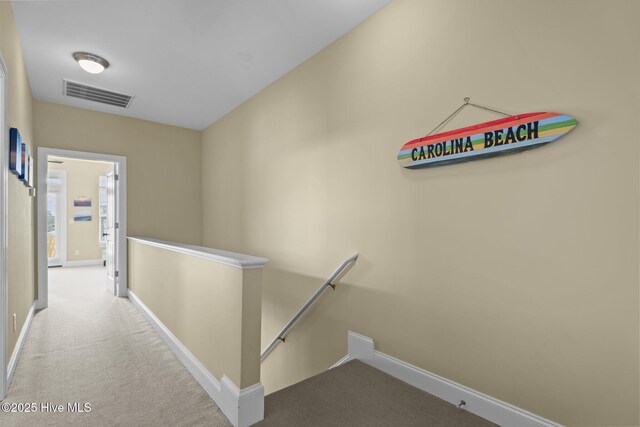 hall with an upstairs landing, visible vents, carpet floors, and baseboards