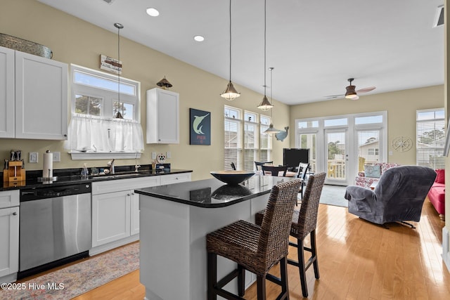kitchen featuring a breakfast bar area, light wood-style flooring, dark countertops, open floor plan, and dishwasher