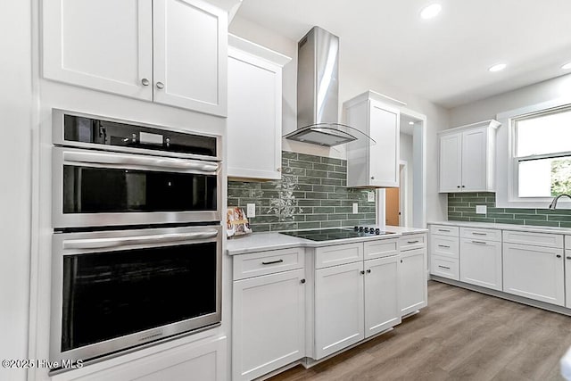 1104 Soundside Rd, Edenton, NC 27932 - kitchen featuring light countertops, stainless steel double oven, white cabinetry, wall chimney range hood, and black electric stovetop