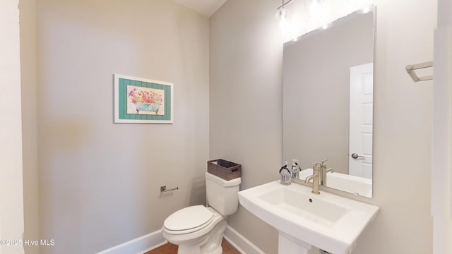 half bath featuring a sink, toilet, baseboards, and wood finished floors