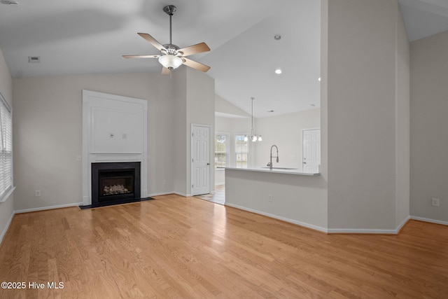 unfurnished living room featuring a fireplace with flush hearth, ceiling fan, light wood-style flooring, a sink, and high vaulted ceiling
