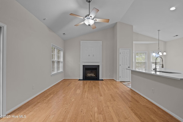 unfurnished living room with a fireplace with flush hearth, a sink, a ceiling fan, light wood finished floors, and baseboards