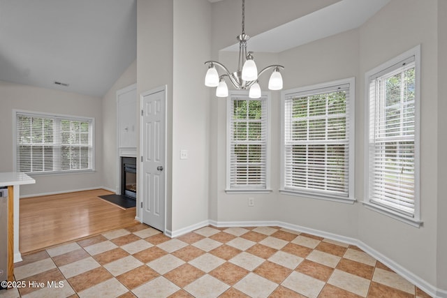 unfurnished dining area with a chandelier, baseboards, a fireplace with flush hearth, and high vaulted ceiling