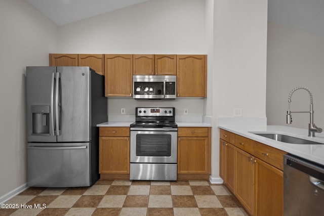 kitchen with stainless steel appliances, a sink, light countertops, brown cabinetry, and baseboards