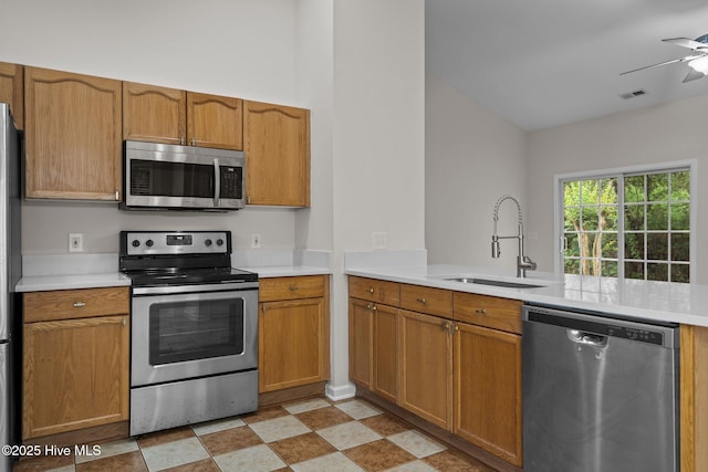kitchen featuring appliances with stainless steel finishes, a sink, a ceiling fan, light countertops, and brown cabinets