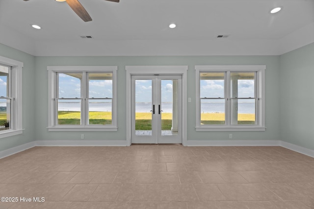 empty room featuring a ceiling fan, french doors, visible vents, baseboards, and a water view