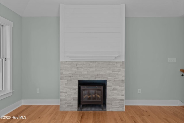 interior details with baseboards, a stone fireplace, and wood finished floors