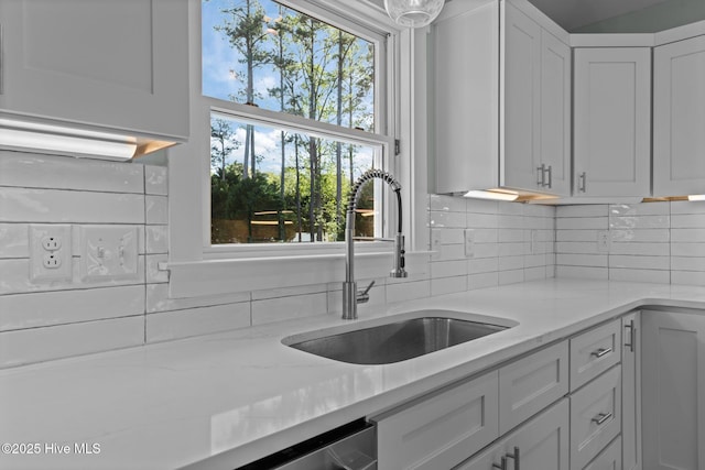 kitchen with backsplash, white cabinets, light stone counters, and a sink