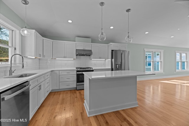 kitchen with appliances with stainless steel finishes, a sink, light countertops, decorative backsplash, and under cabinet range hood
