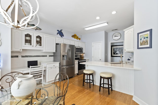 kitchen featuring an inviting chandelier, a kitchen bar, white cabinets, a sink, and stainless steel appliances