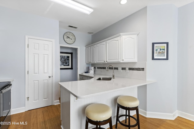 kitchen with a kitchen breakfast bar, visible vents, a sink, light wood finished floors, and white cabinetry