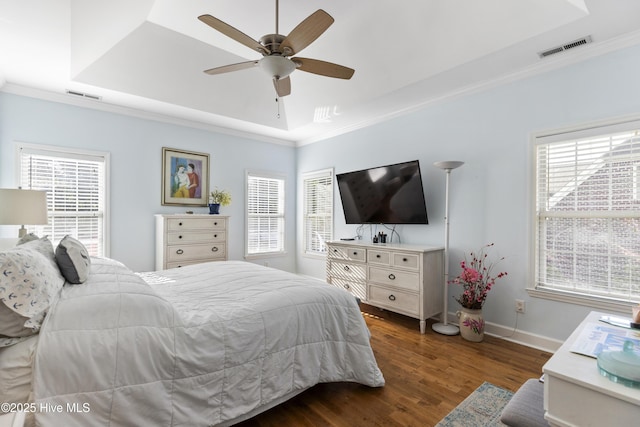 bedroom featuring a raised ceiling, multiple windows, dark wood-type flooring, and visible vents