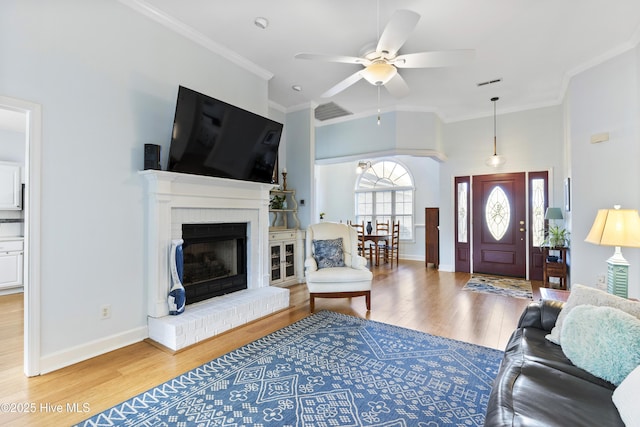 living area featuring ceiling fan, a brick fireplace, baseboards, wood finished floors, and ornamental molding