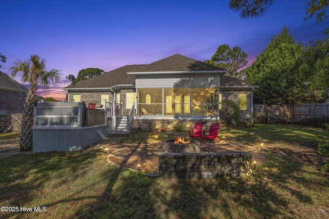 back of property with a fire pit, a fenced backyard, roof with shingles, a sunroom, and a lawn